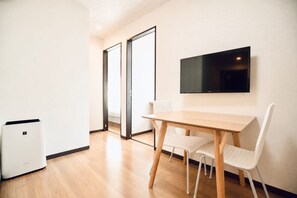 A room with a wooden table, white chairs, a flat-screen TV mounted on the wall, and a white air purifier. - SERENE Osaka | 3 Minutes from Kuromon | 6F-603 | 35 ㎡, 2-Bedroom | Sleeps 4 (Osaka)