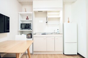Eine kompakte Küche mit weißen Schränken, einer Mikrowelle, einem Kühlschrank und einem Holztisch.