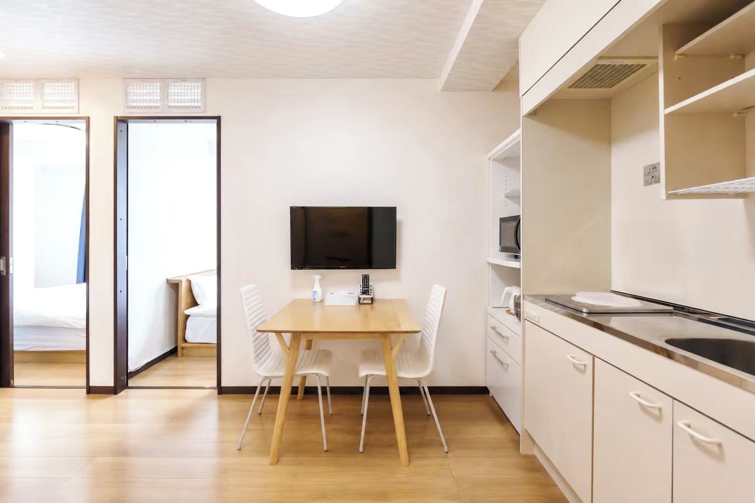 A compact kitchen with a wooden table, white chairs, a flat-screen TV, and a microwave.