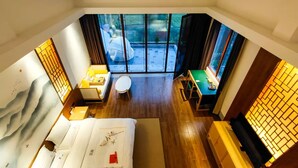 Habitación de hotel con cama, una mesita, una silla y vistas al exterior a través de amplias ventanas.