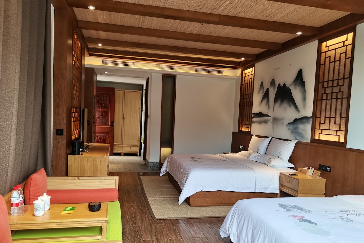 A hotel room with a wooden ceiling, two beds, a desk, and a view of a traditional building.