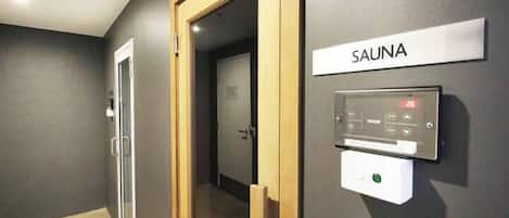 Un pasillo con un letrero de sauna, un panel de control y una puerta que da a otra habitación.