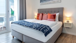 Une chambre moderne avec un grand lit, une tête de lit grise et une vue sur l’extérieur grâce à une porte-fenêtre coulissante.