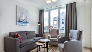 Un salon moderne avec un canapé gris, deux fauteuils, une petite table ronde et un tableau accroché au mur.