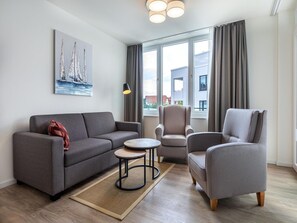 A modern living room with a grey sofa, two armchairs, a small round table, and a painting on the wall. - Parkidylle mit Sauna (Lübeck)