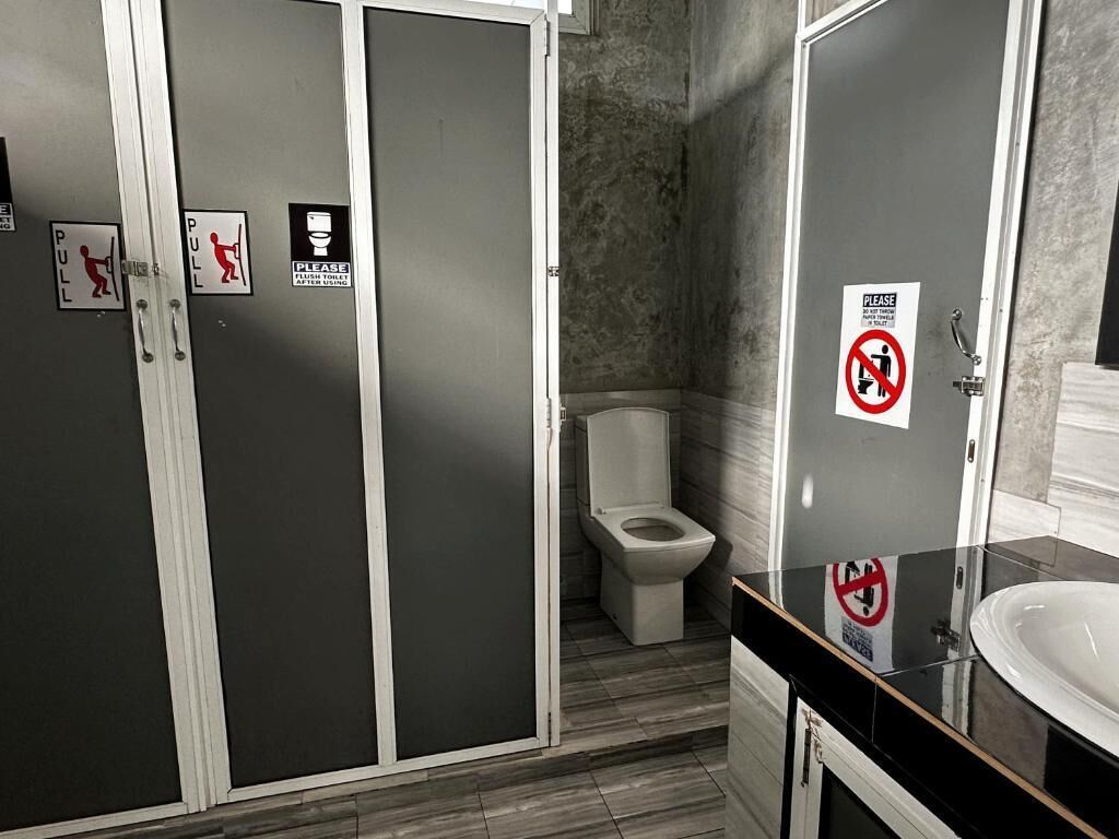 Een badkamer met een toilet, een wastafel en een spiegel. Er staan bordjes op de muren die aangeven waar je aan moet trekken en waar niet aan mag zitten.