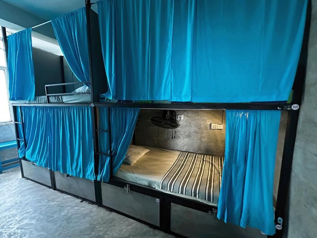 A bunk bed with curtains, a power outlet, and a wall-mounted shelf.