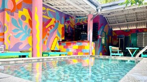 Una piscina con un colorido mural en las paredes, una zona de estar cubierta y un pequeño bar.