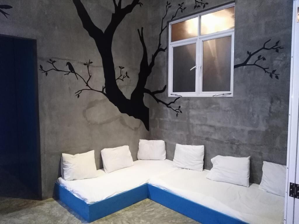 A room with a blue sectional sofa against a wall with a tree mural and a window.