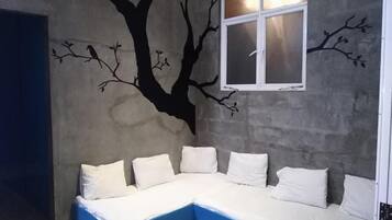 A room with a blue sectional sofa against a wall with a tree mural and a window.