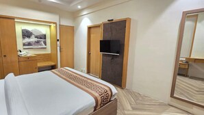 A hotel room with a bed, a wardrobe, a desk, a television, and a mirror.