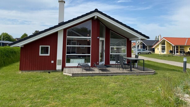 A red building with a sloped roof, large windows, and a covered patio area with outdoor furniture.