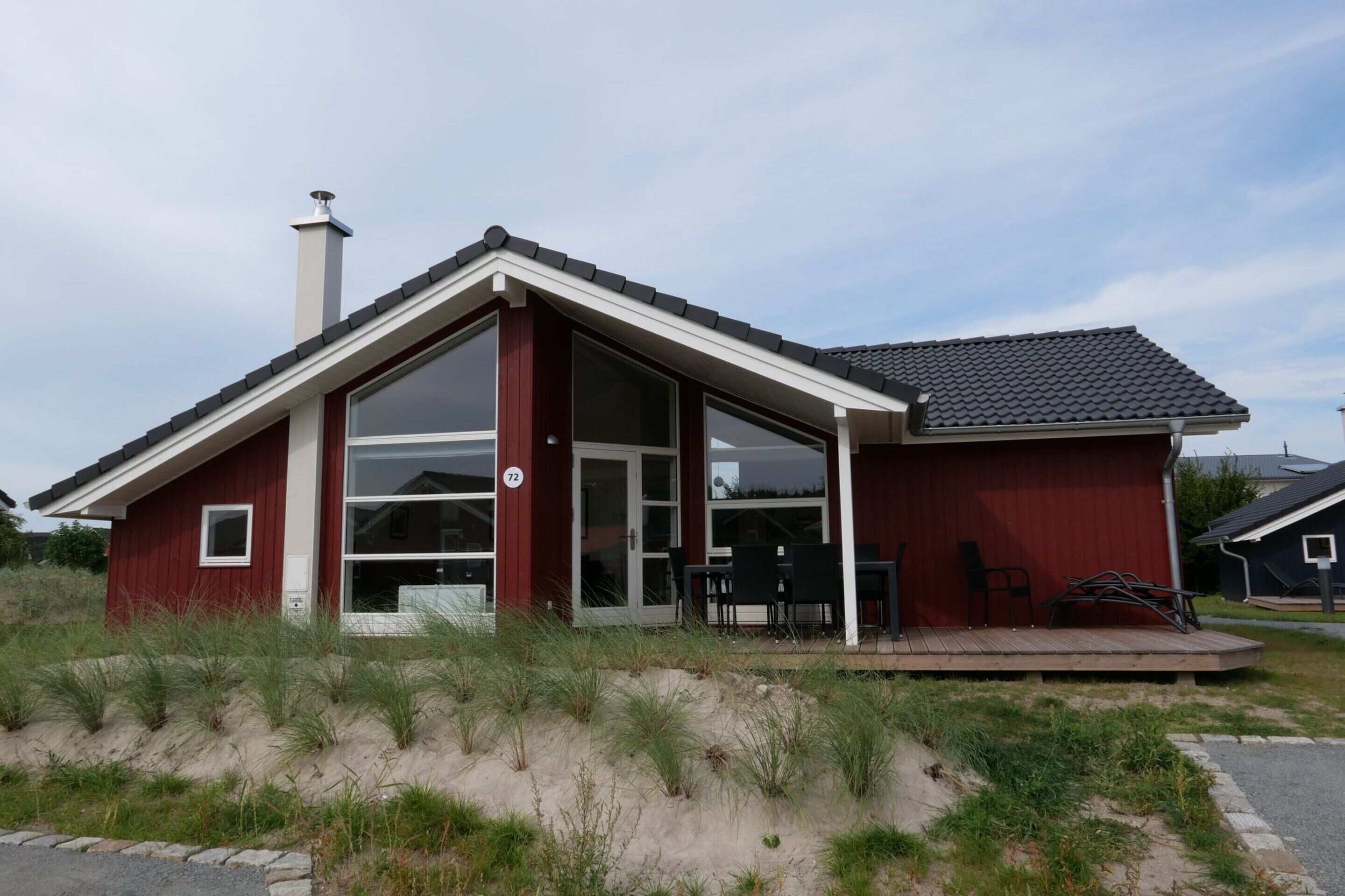 A red building with a large glass door and windows, a chimney, and a small outdoor seating area with chairs.