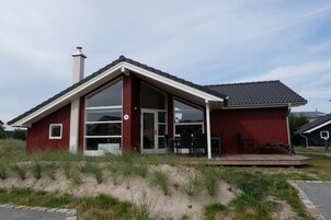 A red building with a large glass door and windows, a chimney, and a small outdoor seating area with chairs.