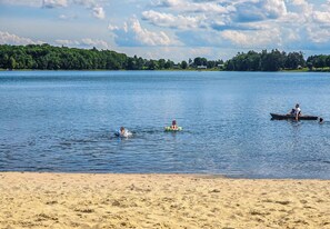 Une plage avec une eau calme, un rivage sablonneux et une ligne d’arbres à l’horizon.