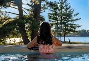 A person sitting by a pool with a view of trees and a body of water.