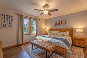 Ein Schlafzimmer mit Bett, Sitzbank, Nachttischen, Deckenventilator und Bildern an den Wänden.