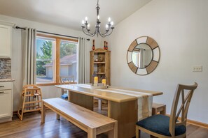 Ein Essbereich mit Holztisch, einer Bank, Stühlen, einer Kristallleuchter, einem Spiegel und einem Fenster mit Vorhängen.