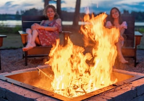 Two people sitting on chairs by a fire pit with a lake in the background.