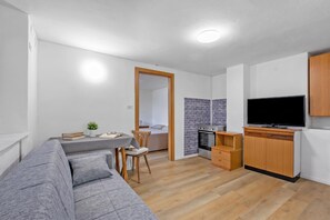 Ein modernes Wohnzimmer mit grauem Sofa, einem Esstisch mit Stühlen, einem Fernseher und einer Küchenzeile inklusive Herd und Backofen.