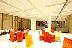 Amplio espacio interior con filas de sillas y mesas, un mostrador de recepción y un escenario decorado con flores.