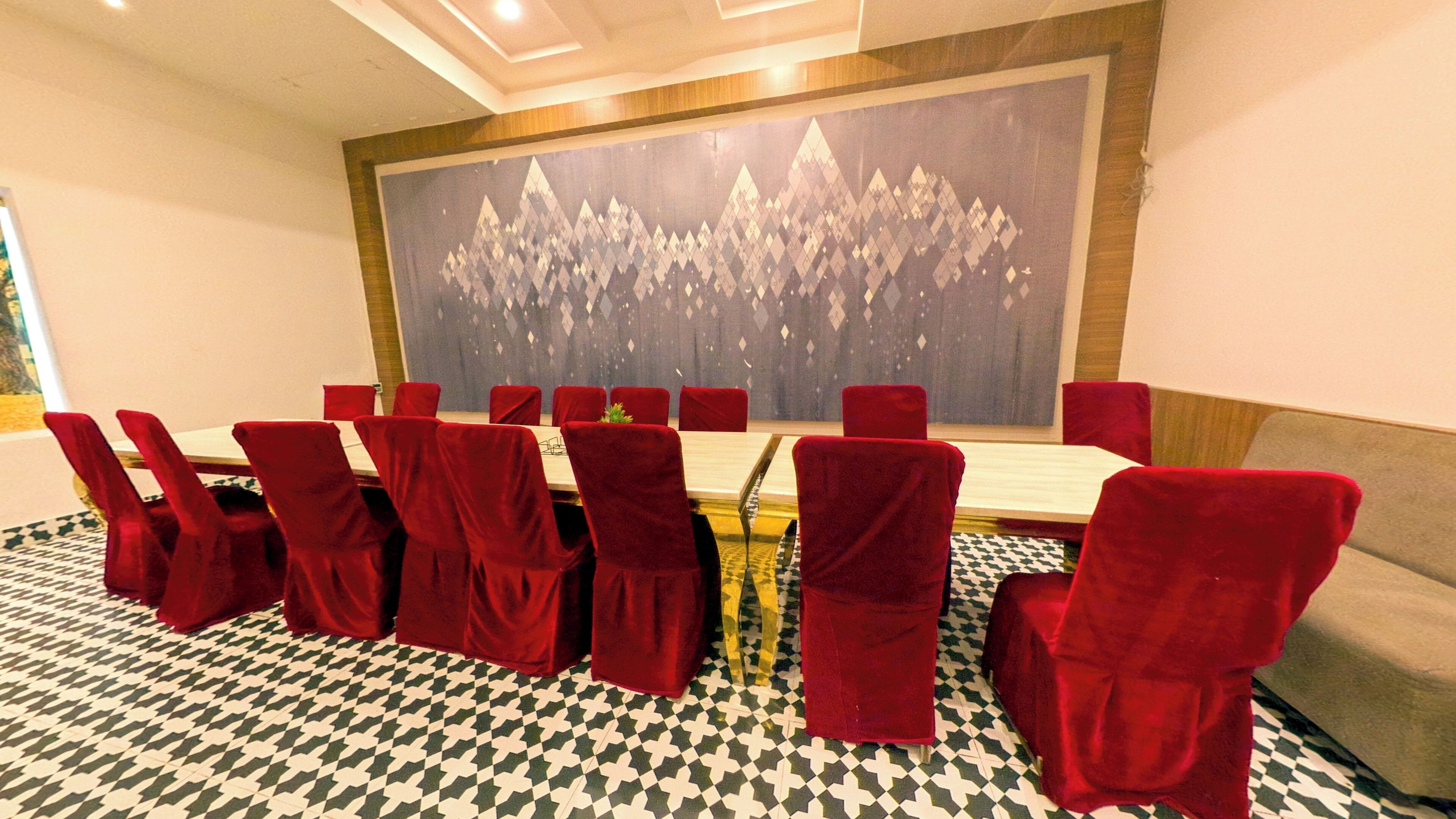 Une salle de conférence avec une longue table et des chaises rouges, un grand tableau abstrait au mur et un revêtement de sol en moquette à motifs.