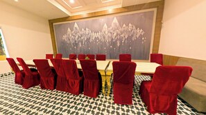 A conference room with a long table and red chairs, a large abstract painting on the wall, and patterned carpet flooring. - Goldys Hotel Banquets & Restaurant (Hisar)