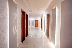 Un largo pasillo bien iluminado con paredes de mármol y puertas de madera, que conduce a una habitación con un ventanal grande.