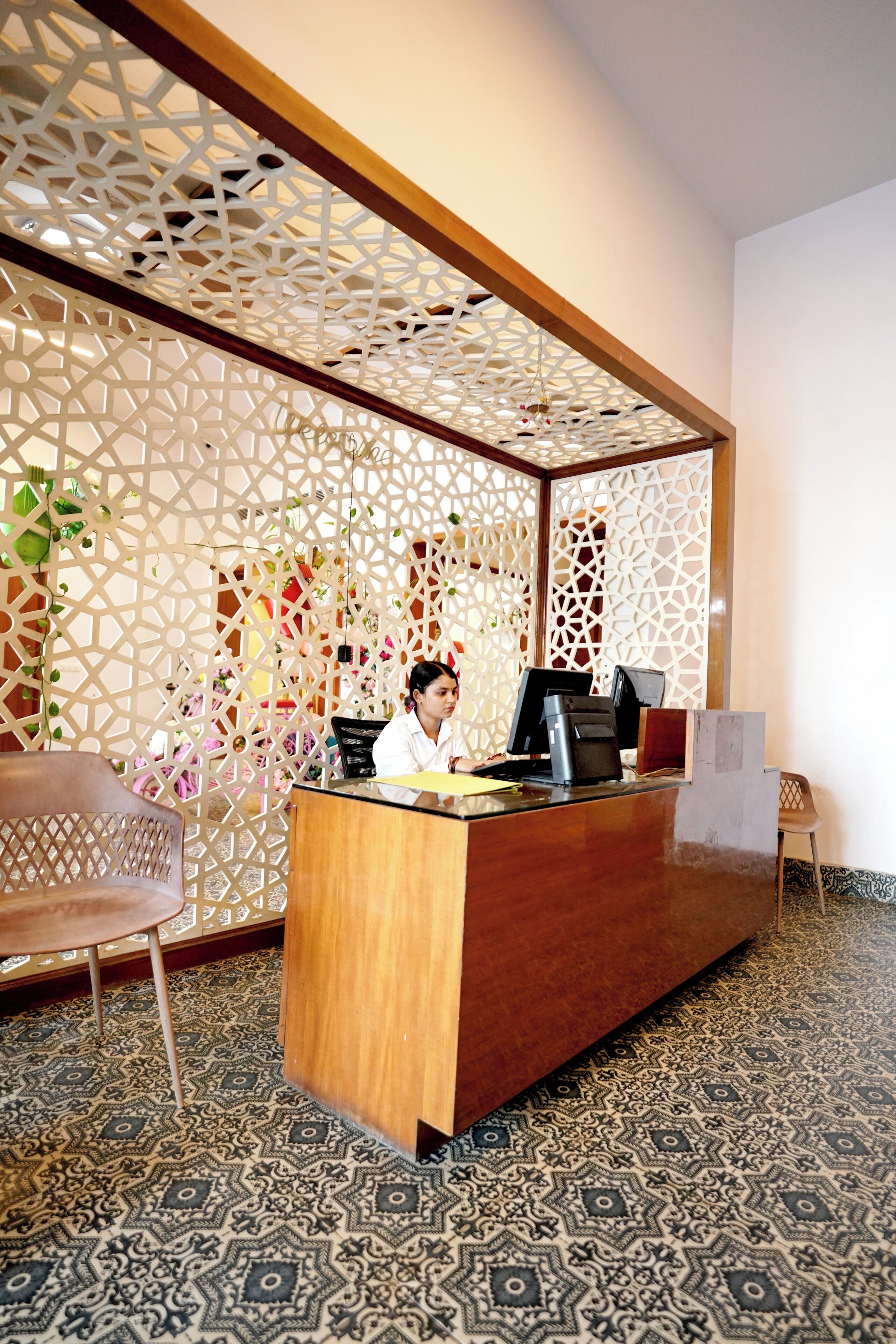A reception desk with a wooden finish, a computer monitor, and a cash register. There is a patterned floor and a decorative partition with geometric designs.