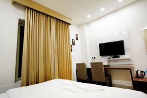 Habitación de hotel con una cama, televisión, escritorio y dos sillas, además de una ventana con cortinas.