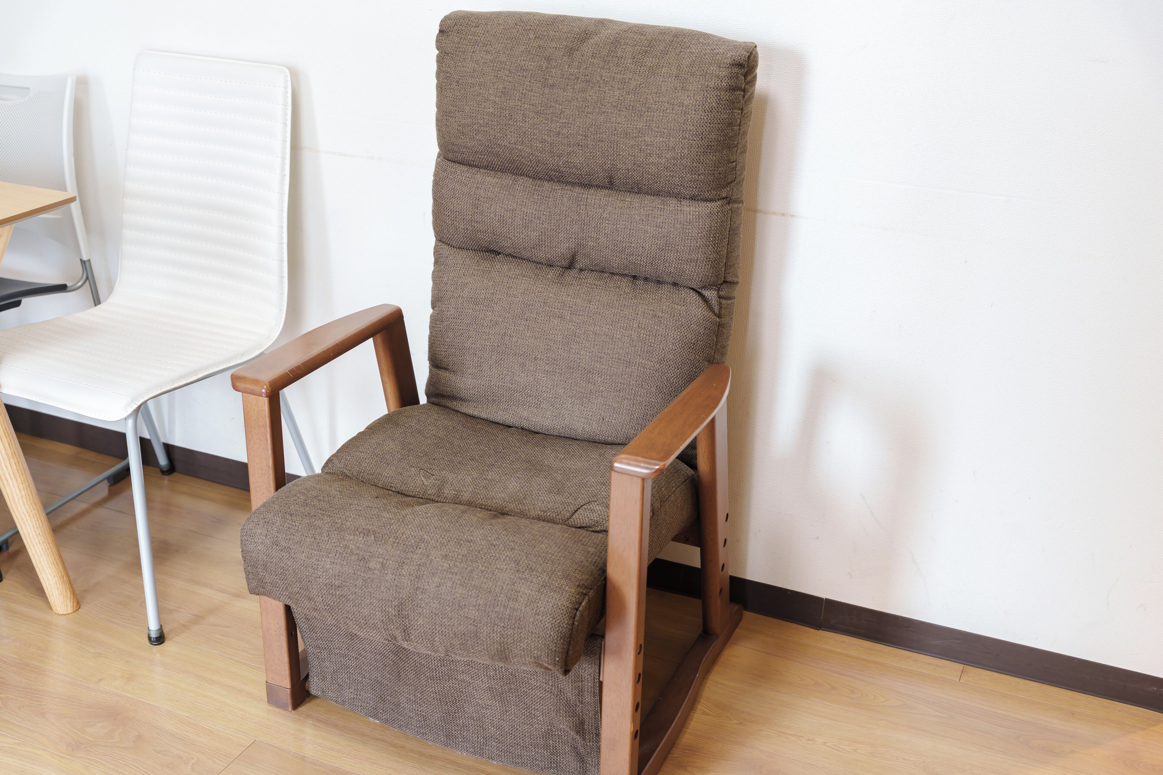 A wooden chair with a cushioned seat and backrest, positioned against a white wall with a wooden floor.