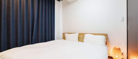 Une chambre d’hôtel avec un grand lit, une tête de lit en bois, une table de chevet avec une lampe et des rideaux foncés.