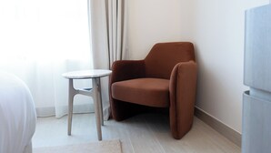 A corner of a room with a brown chair, a small round table, and a light-colored floor. - Bloomfields 1BR in Vantage 2 - Yas Golf (Abu Dhabi)