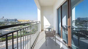A balcony with a table and chairs, a view of a cityscape, and a clear sky. - Bloomfields 1BR in Vantage 2 - Yas Golf (Abu Dhabi)
