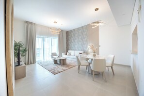 A modern living room with a sofa, coffee table, and dining area with chairs. - Bloomfields 1BR in Vantage 2 - Yas Golf (Abu Dhabi)