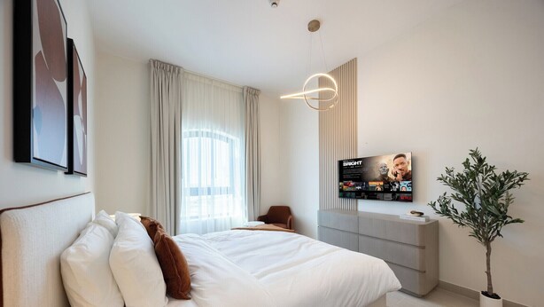 A modern hotel room with a large bed, a TV mounted on the wall, a desk, and a potted plant. - Bloomfields 1BR in Vantage 2 - Yas Golf (Abu Dhabi)