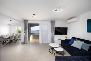Ein modernes Wohnzimmer mit einem dunklen Sofa, einem Flachbildfernseher und einem Essbereich mit Stühlen und einem Tisch.