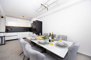 Eine moderne Küche mit weißen Schränken, einem schwarzen Kühlschrank und einem Essbereich mit einem für vier Personen gedecktem Tisch.