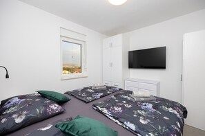 Ein Schlafzimmer mit zwei Betten, einem Fenster, einem Flachbildfernseher und einem weißen Kleiderschrank.