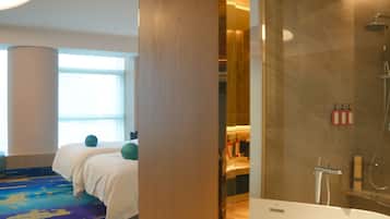A hotel room with a bed, a bathroom with a shower, and a large window.