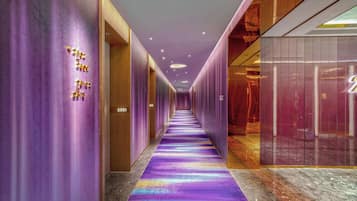 A hotel corridor with purple walls, numbered doors, and a multicolored carpet.