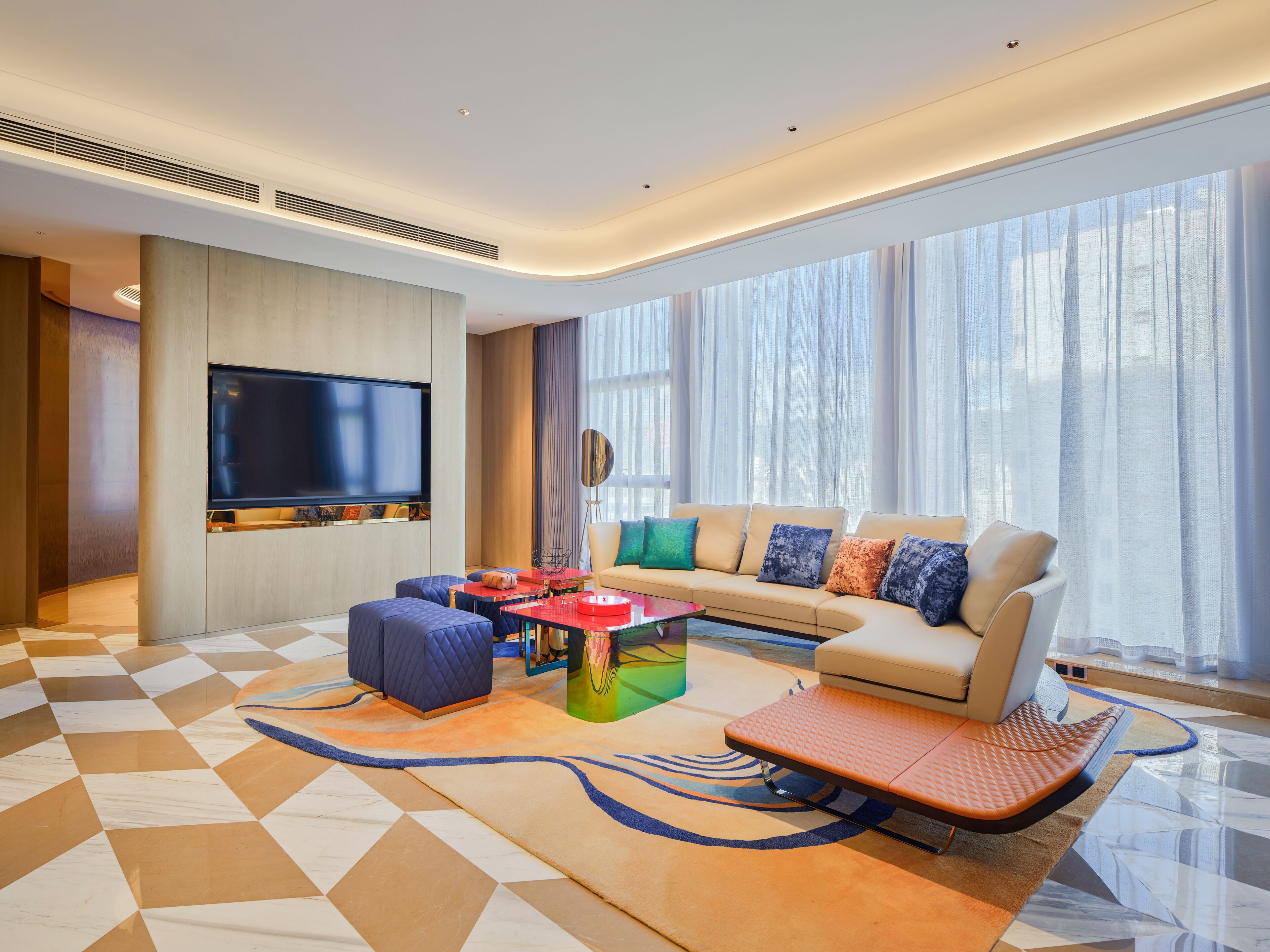 Una sala de estar moderna con un televisor de pantalla plana, un sofá, otomanas y una mesa de centro.
