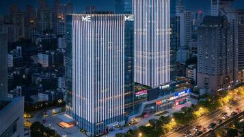 Un moderno edificio de gran altura con líneas verticales y señalización iluminada, rodeado de un paisaje urbano nocturno.
