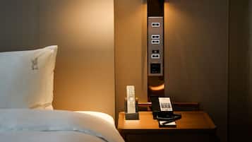 A hotel room with a bed, a bedside table with a lamp, a remote control, and a telephone.