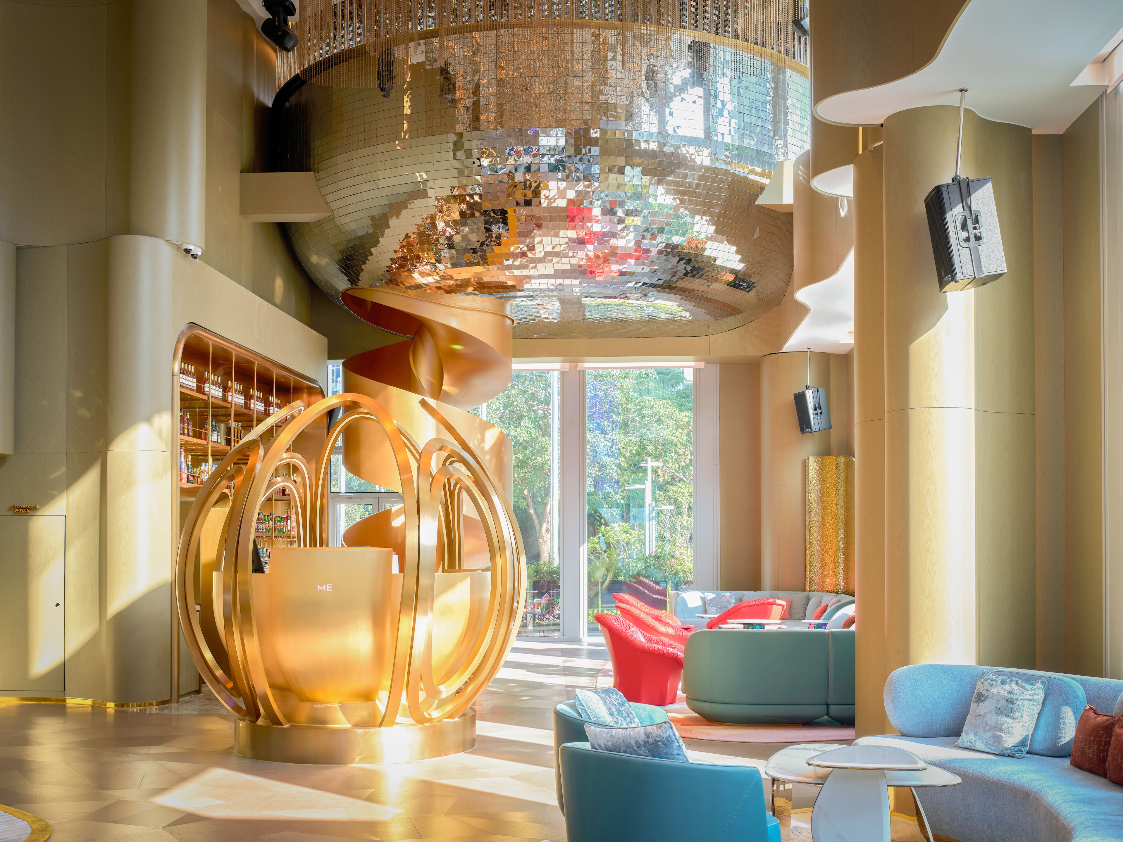 Een modern interieur met een ronde metalen sculptuur, een zithoek met banken, en een groot raam met uitzicht op groen.