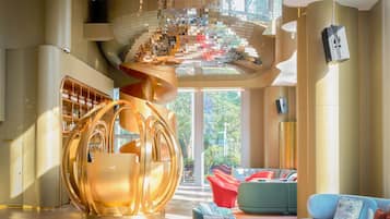 Een modern interieur met een ronde metalen sculptuur, een zithoek met banken, en een groot raam met uitzicht op groen.