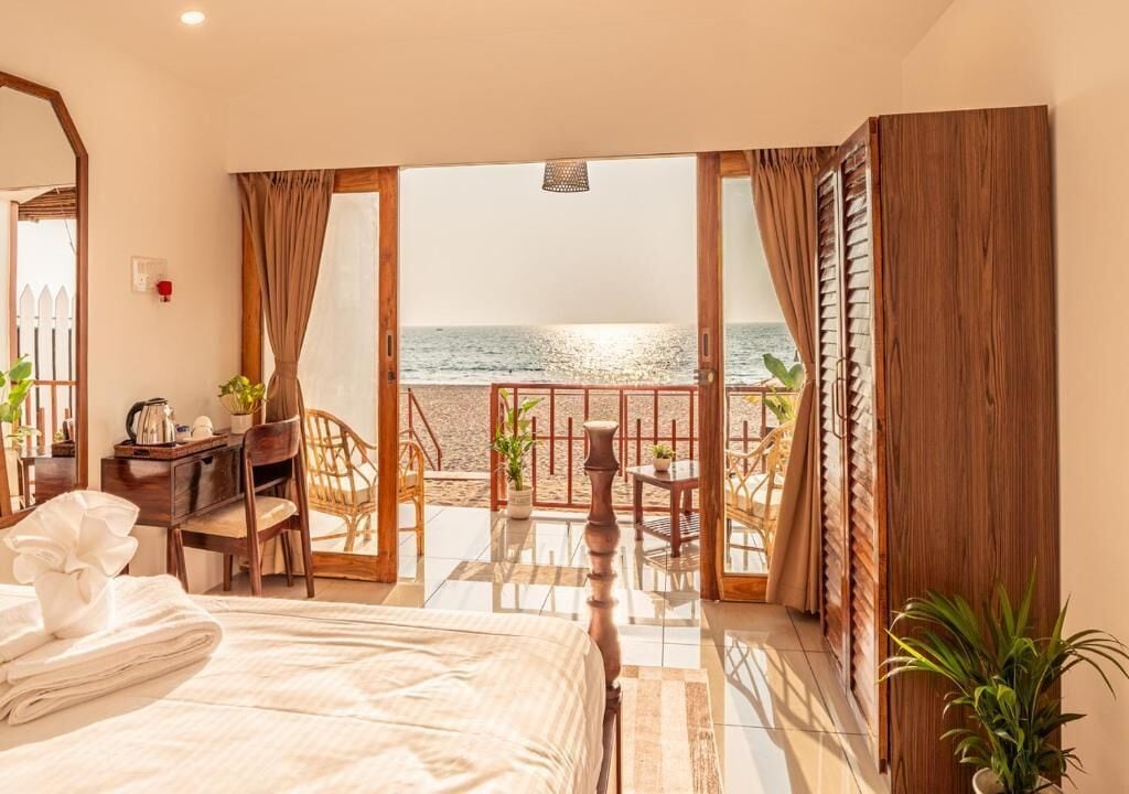 Quarto de hotel com uma cama, escrivaninha, cadeira, mesa pequena e vista para o mar.