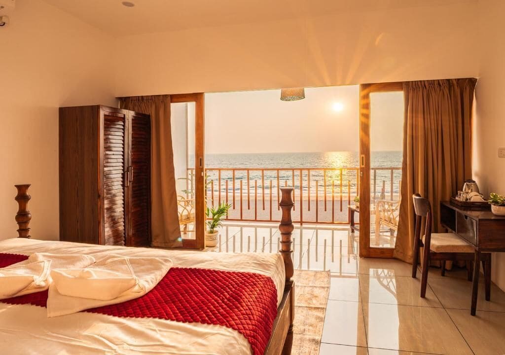 Quarto de hotel com cama, escrivaninha e varanda vista para o mar.
