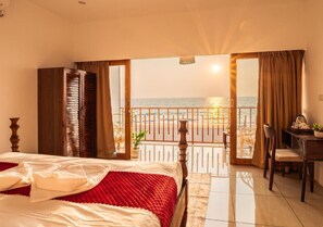 A hotel room with a bed, a desk, and a balcony with a view of the sea. - Ananas Beach Resort (Agonda)