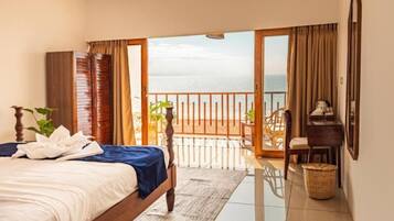 Habitación de hotel con cama, escritorio, silla, balcón con vistas al mar y ventana con cortinas.